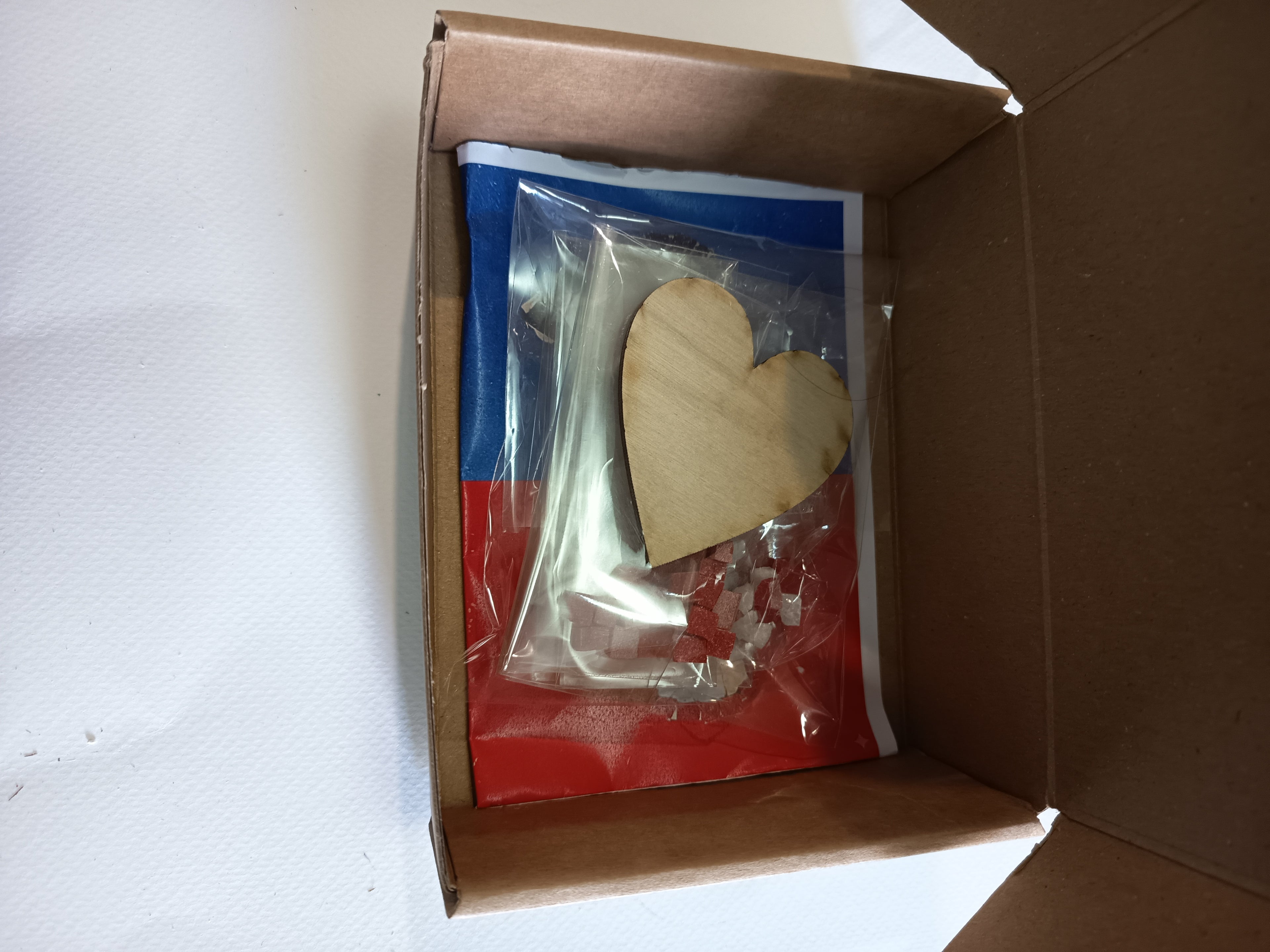 Cardboard box with a wooden heart cutout and other items on a white background